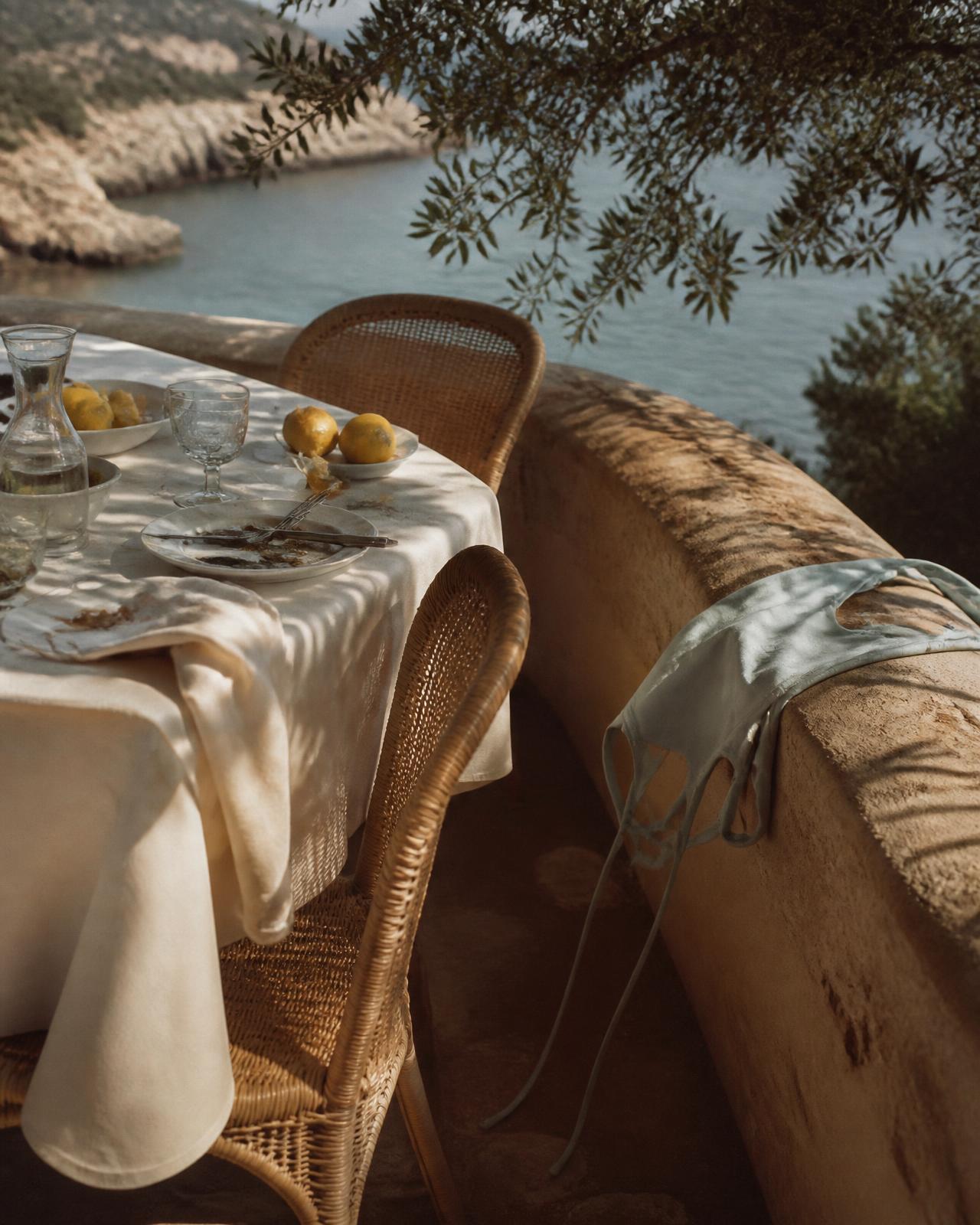 A long lunch table in ivory linen above the sea in late afternoon light